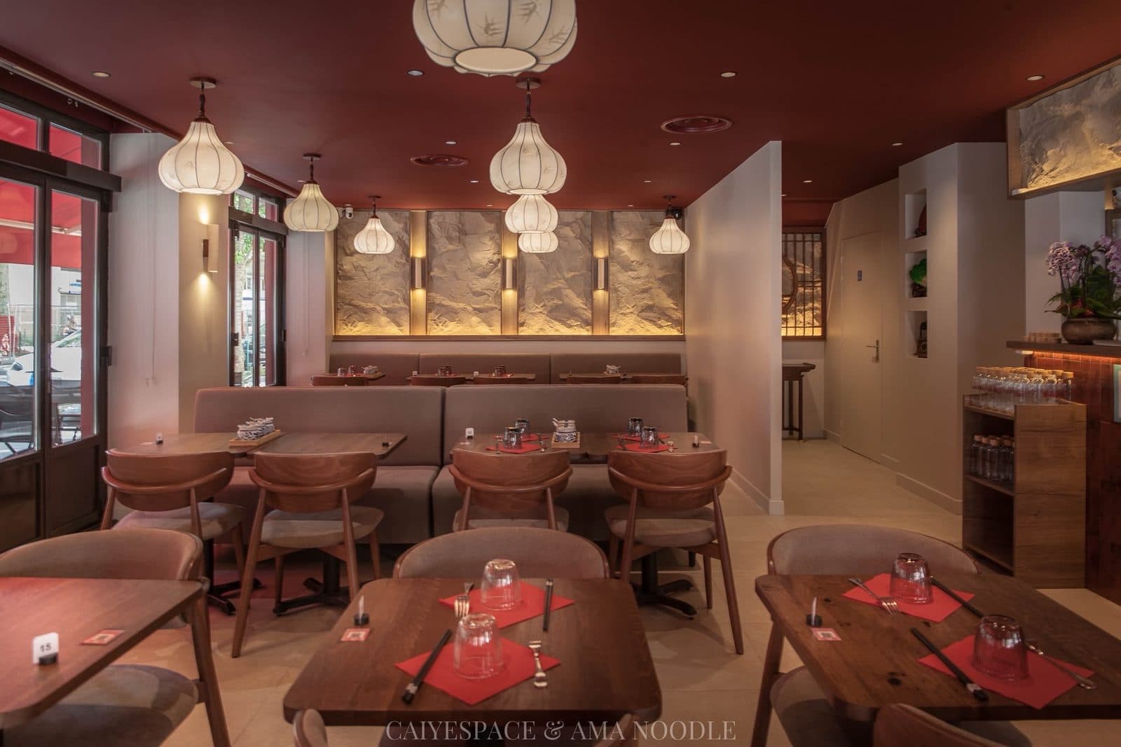 La salle d'Ama Noodle : lanternes blanches, bois et banquettes, tables dressées